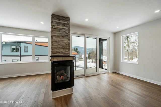 unfurnished living room featuring baseboards, wood finished floors, a fireplace, a mountain view, and recessed lighting