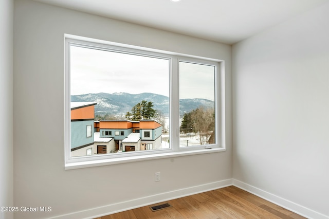 empty room with visible vents, a mountain view, baseboards, and wood finished floors