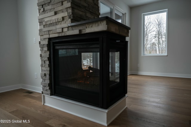 room details featuring visible vents, baseboards, wood finished floors, and a stone fireplace