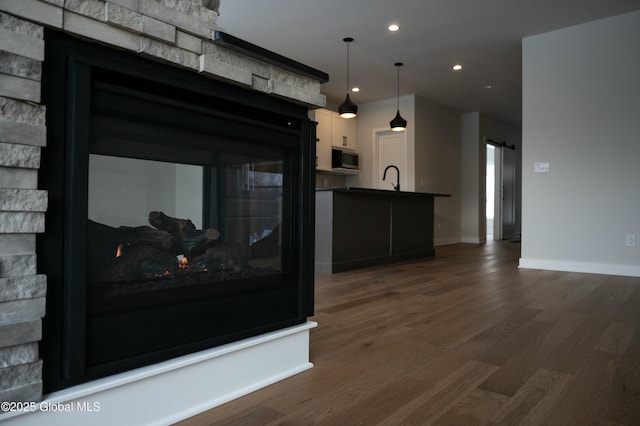 interior space featuring dark wood-style floors, decorative light fixtures, dark countertops, stainless steel microwave, and a barn door