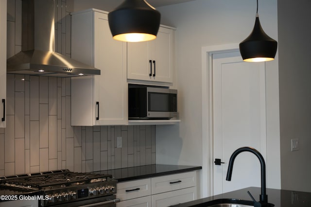 kitchen featuring gas range oven, stainless steel microwave, backsplash, white cabinetry, and wall chimney exhaust hood