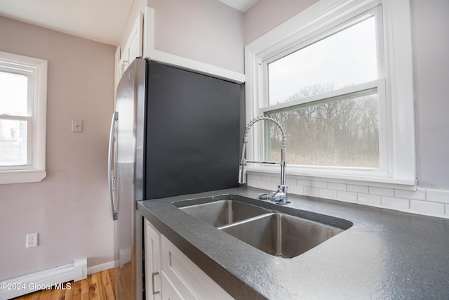 kitchen with stainless steel fridge, light wood-type flooring, baseboard heating, sink, and white cabinets