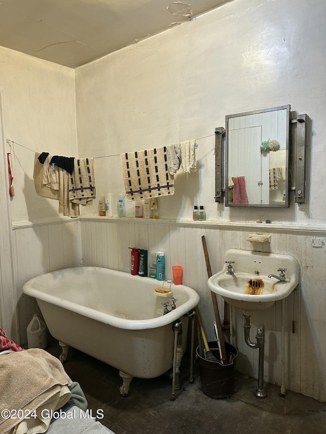 bathroom with sink, concrete floors, a bathing tub, and wood walls