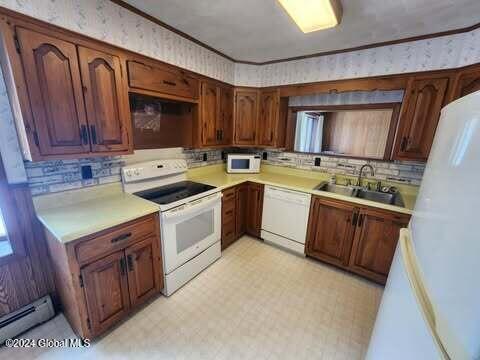 kitchen with white appliances, baseboard heating, crown molding, and sink