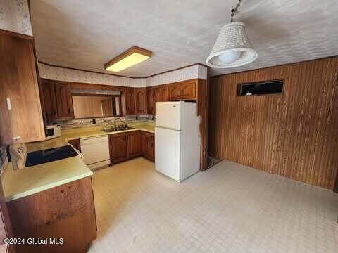 kitchen featuring pendant lighting, white appliances, wooden walls, and sink