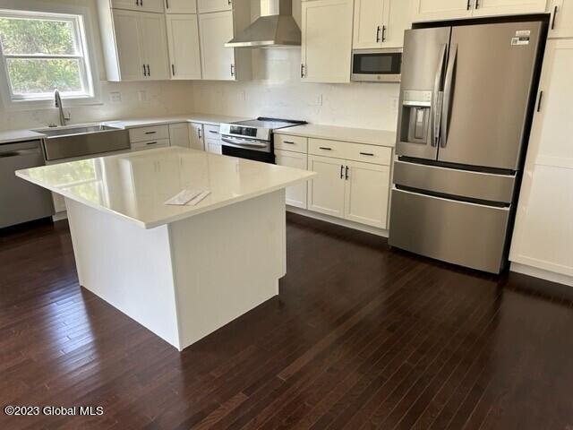 kitchen with appliances with stainless steel finishes, dark hardwood / wood-style floors, a kitchen island, and wall chimney exhaust hood