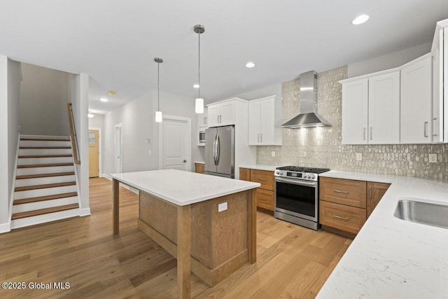 kitchen featuring wall chimney exhaust hood, hanging light fixtures, appliances with stainless steel finishes, a kitchen island, and white cabinets