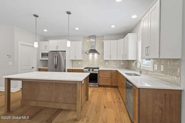 kitchen featuring wall chimney exhaust hood, sink, appliances with stainless steel finishes, a kitchen island, and white cabinets