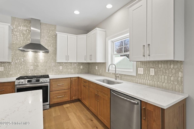 kitchen with wall chimney range hood, sink, appliances with stainless steel finishes, light stone counters, and white cabinets