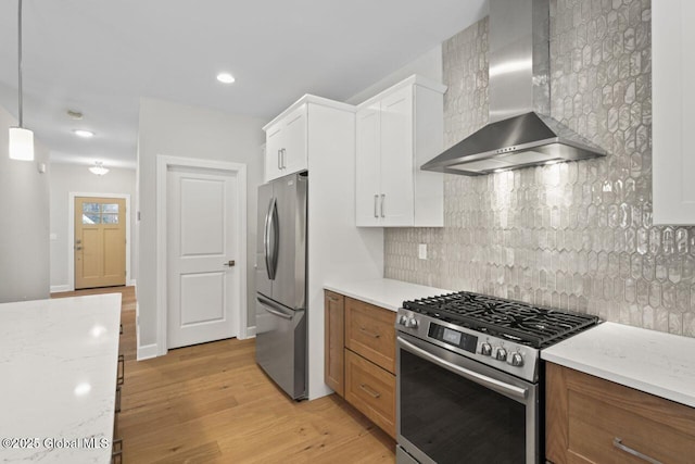 kitchen featuring appliances with stainless steel finishes, hanging light fixtures, light stone countertops, white cabinets, and wall chimney exhaust hood