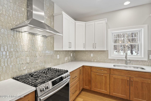 kitchen with sink, white cabinetry, stainless steel range with gas stovetop, tasteful backsplash, and wall chimney exhaust hood