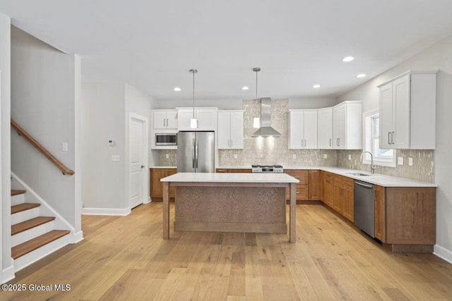 kitchen with wall chimney range hood, sink, appliances with stainless steel finishes, hanging light fixtures, and a kitchen island