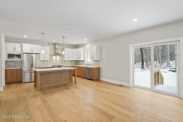 kitchen with a kitchen island, white cabinets, hanging light fixtures, stainless steel appliances, and wall chimney exhaust hood