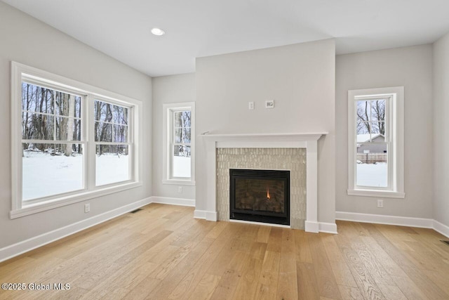 unfurnished living room featuring a tiled fireplace and light wood-type flooring