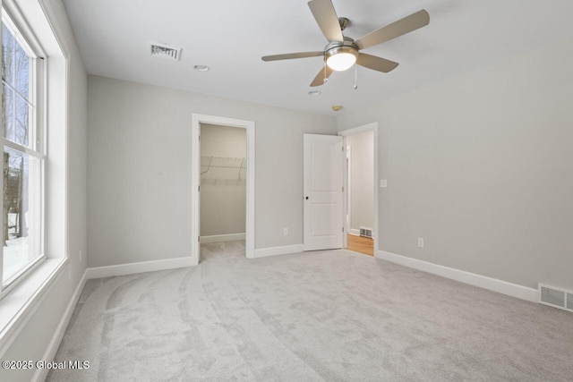 unfurnished bedroom featuring multiple windows, a walk in closet, light carpet, and ceiling fan