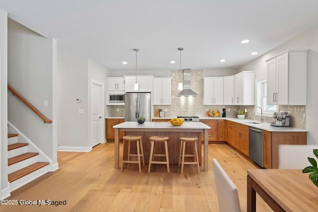 kitchen featuring white cabinetry, a center island, hanging light fixtures, appliances with stainless steel finishes, and wall chimney range hood