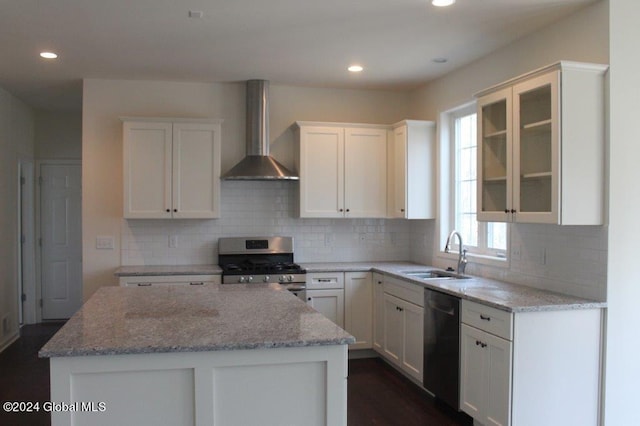 kitchen with light stone countertops, stainless steel appliances, wall chimney range hood, white cabinets, and a center island