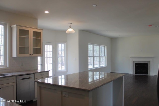 kitchen with light stone countertops, a center island, dark wood-type flooring, stainless steel dishwasher, and decorative light fixtures