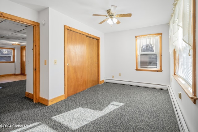 unfurnished bedroom featuring a closet, dark carpet, baseboard heating, and ceiling fan