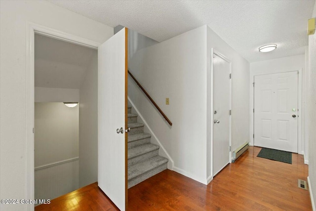 stairs with hardwood / wood-style floors, a textured ceiling, and a baseboard radiator