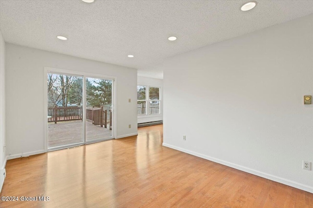 empty room with a textured ceiling, light hardwood / wood-style floors, and a baseboard heating unit