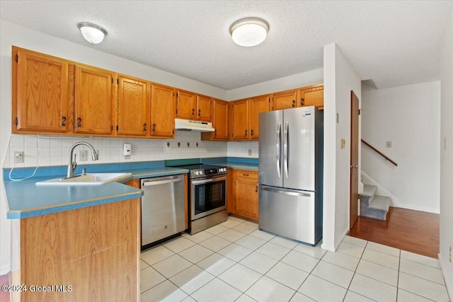 kitchen featuring sink, decorative backsplash, a textured ceiling, appliances with stainless steel finishes, and light tile patterned flooring