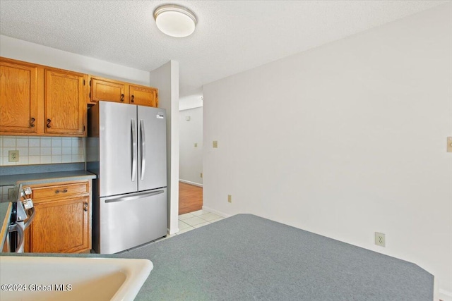 kitchen with a textured ceiling, light tile patterned floors, backsplash, and appliances with stainless steel finishes