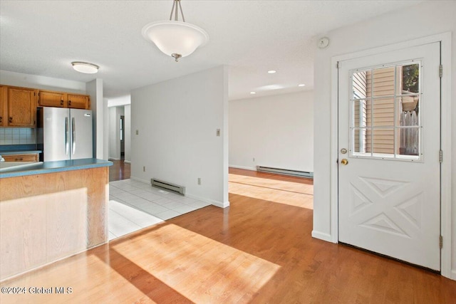 kitchen with baseboard heating, stainless steel refrigerator, decorative light fixtures, and light wood-type flooring