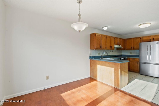 kitchen featuring stainless steel refrigerator, sink, light hardwood / wood-style flooring, kitchen peninsula, and pendant lighting