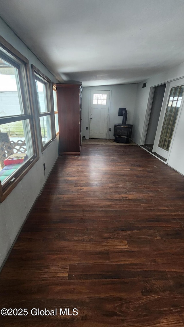 unfurnished living room featuring dark wood-type flooring, a wealth of natural light, and a wood stove