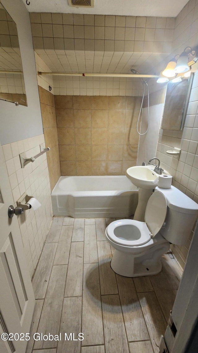 full bathroom featuring toilet, sink, tile walls, and tiled shower / bath combo