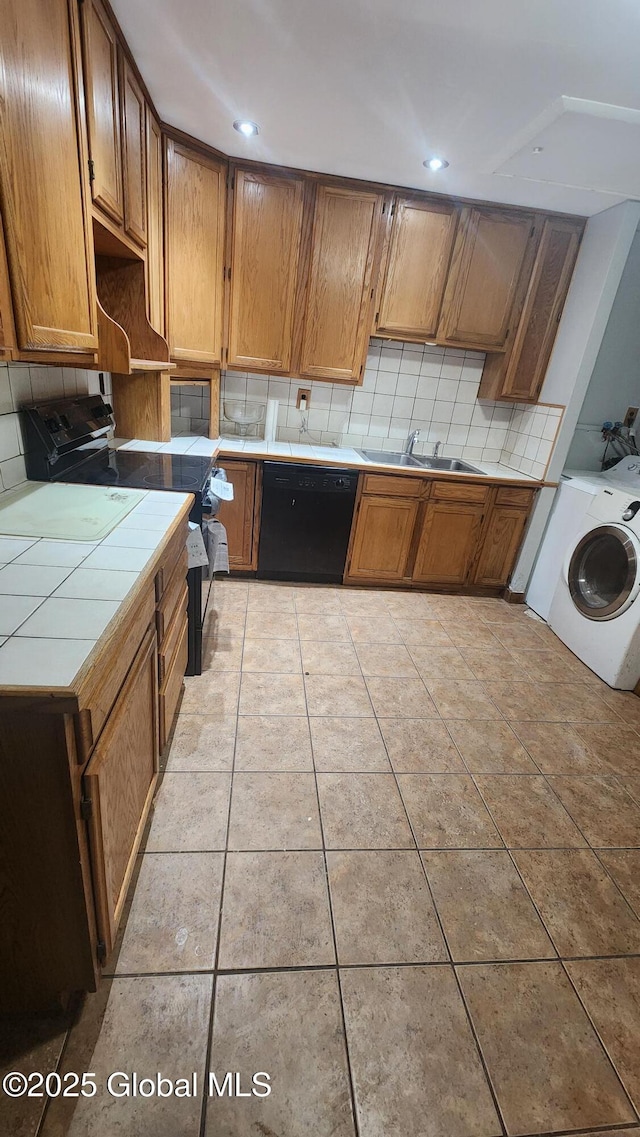 kitchen with washer / clothes dryer, black appliances, light tile patterned floors, tile countertops, and sink