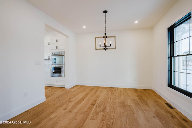 unfurnished dining area with a chandelier and light hardwood / wood-style floors