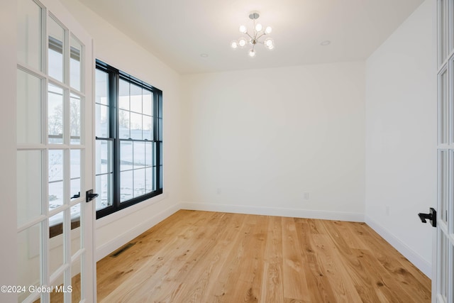 empty room featuring light wood-type flooring, a wealth of natural light, and an inviting chandelier