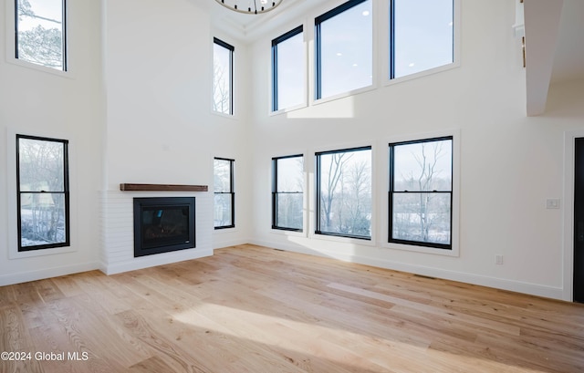 unfurnished living room with a fireplace, a high ceiling, light hardwood / wood-style floors, and a wealth of natural light