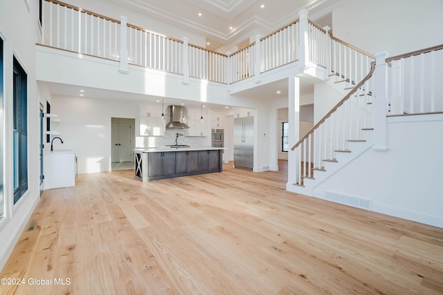 unfurnished living room featuring a high ceiling, light hardwood / wood-style floors, and sink