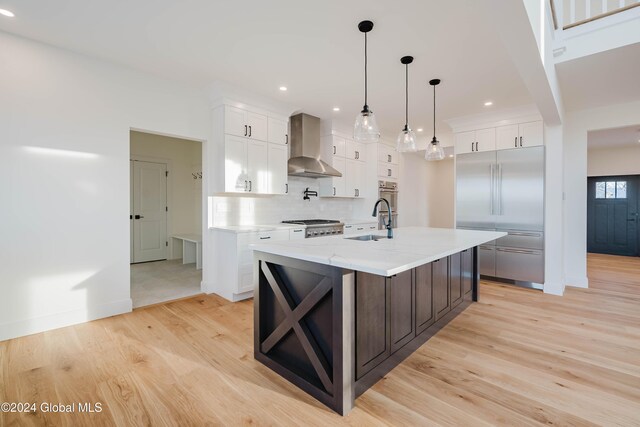 kitchen with white cabinetry, an island with sink, light hardwood / wood-style floors, and wall chimney range hood