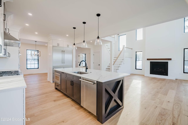 kitchen with white cabinetry, sink, stainless steel appliances, an island with sink, and decorative light fixtures