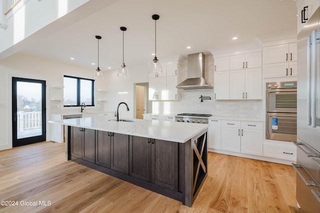 kitchen with white cabinets, wall chimney exhaust hood, an island with sink, and appliances with stainless steel finishes