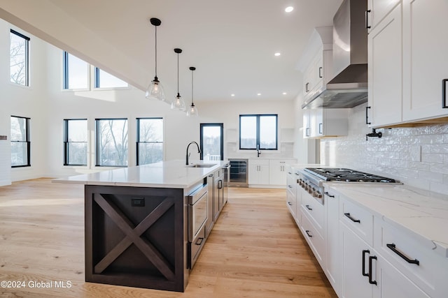 kitchen featuring wall chimney range hood, stainless steel gas cooktop, light stone counters, a spacious island, and white cabinets