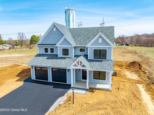 view of front of house with central AC unit, aphalt driveway, covered porch, an attached garage, and roof with shingles