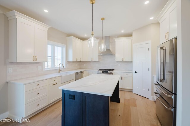 kitchen featuring light wood-type flooring, stainless steel appliances, a sink, and wall chimney range hood