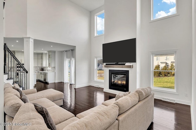 living room featuring a towering ceiling, dark hardwood / wood-style floors, and ornate columns