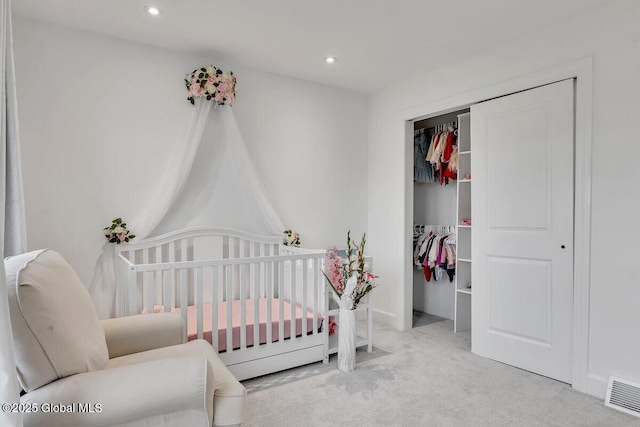 bedroom with a crib, light colored carpet, and a closet