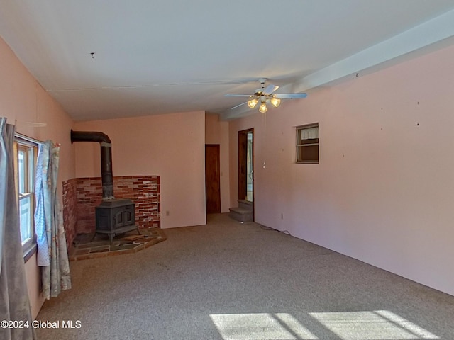 unfurnished living room with carpet, vaulted ceiling, a wood stove, and ceiling fan