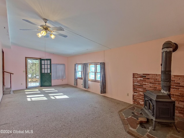 unfurnished living room featuring carpet, vaulted ceiling, a wood stove, and ceiling fan