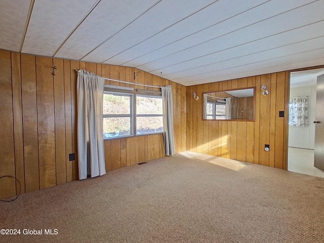 spare room featuring carpet flooring, wood walls, and vaulted ceiling