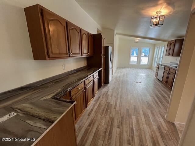 kitchen with vaulted ceiling, stainless steel appliances, hanging light fixtures, and light hardwood / wood-style flooring