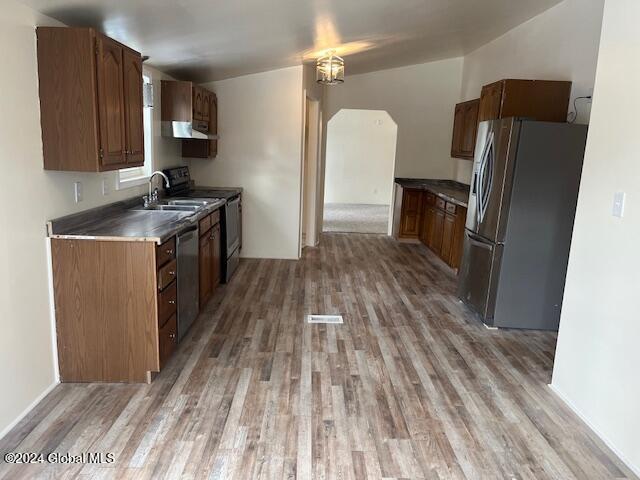 kitchen featuring appliances with stainless steel finishes, ventilation hood, sink, light hardwood / wood-style floors, and lofted ceiling