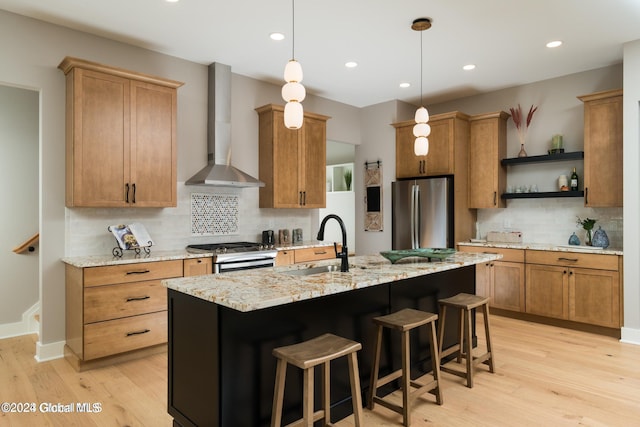 kitchen featuring a center island with sink, hanging light fixtures, stainless steel appliances, wall chimney range hood, and open shelves